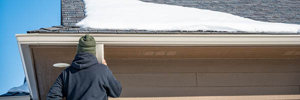 Man checks the gutters of his home for ice dams.